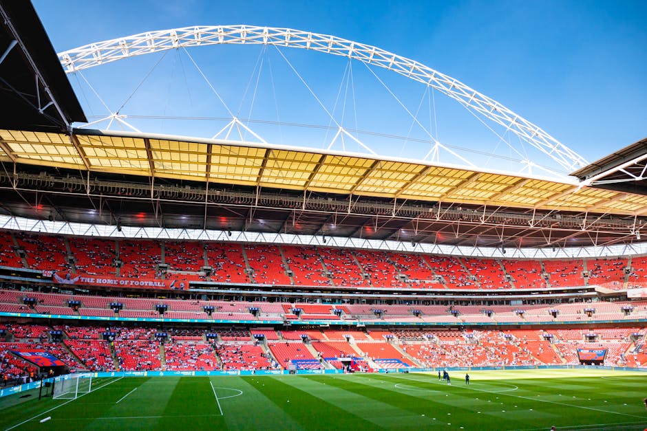 An empty stadium seating area with rows of coral-colored plastic chairs, illuminated by natural light. The chairs are arranged in multiple tiers, with a central aisle running down the middle. The surf